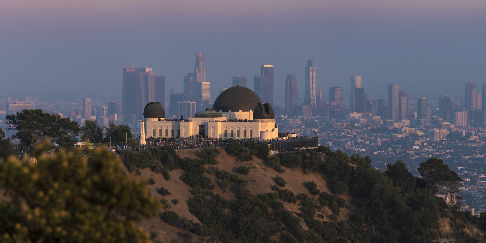 Photo of the exterior of the Griffith Observatory with Downtown Los Angeles lit up in the background.