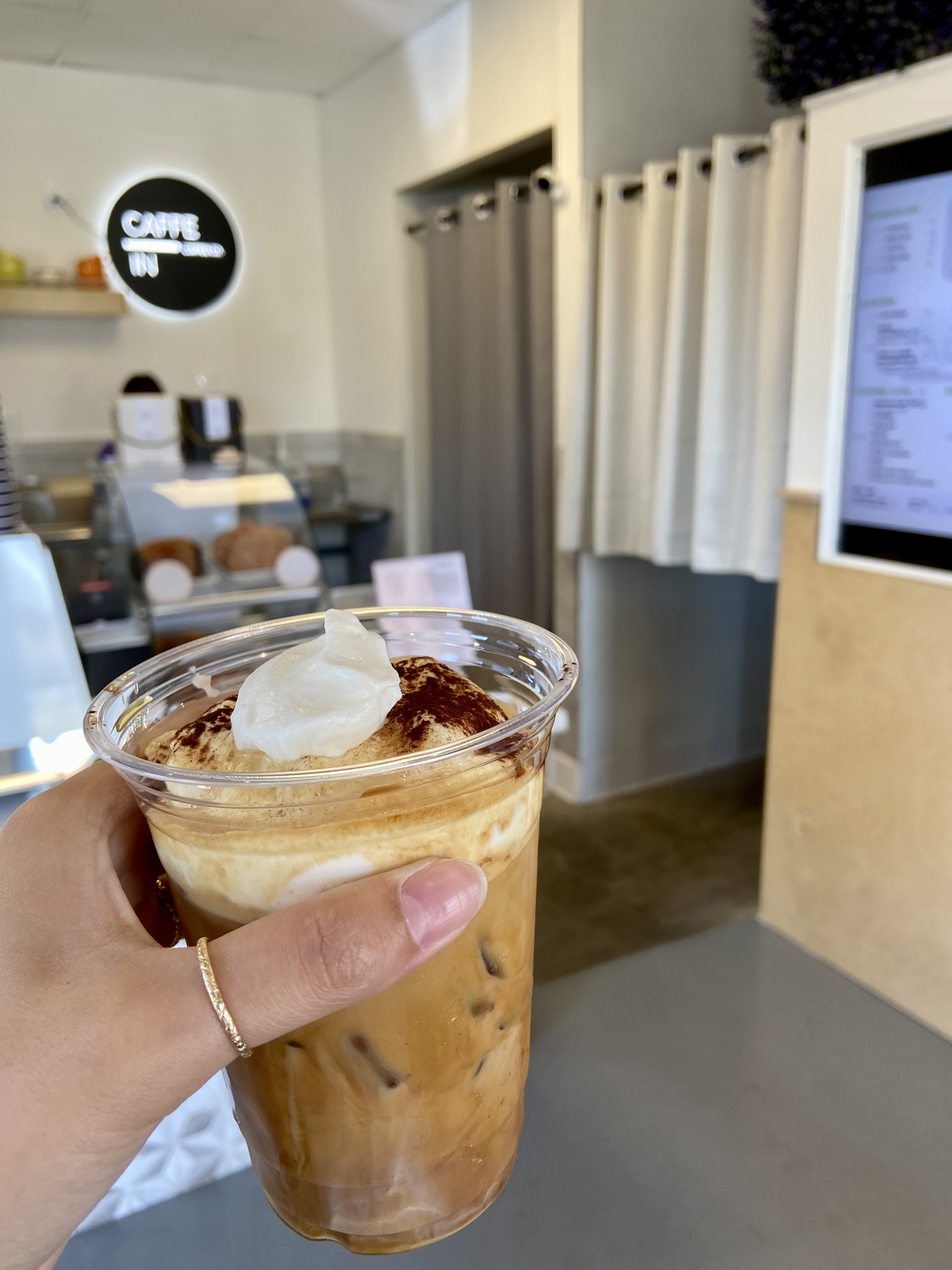 Photo of a hand holding an iced coffee drink with the interior of a coffee shop in the background.