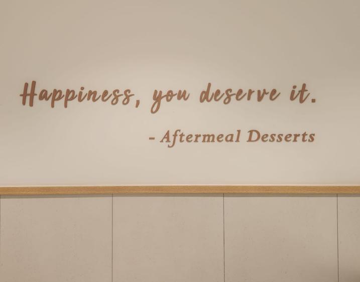 In image of a quote on a wall that reads "Happiness, you deserve it" attributed to Aftermeal Desserts.