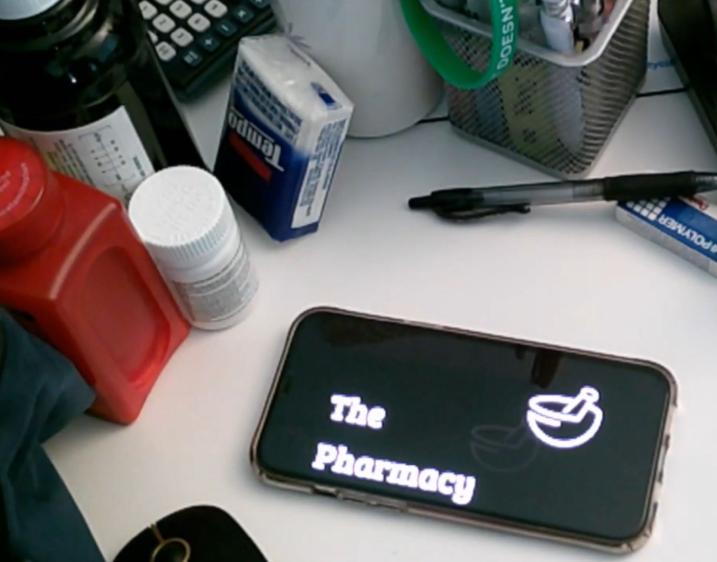 Photo of a phone screen with the words "the pharmacy" surrounded by pill bottles and office supplies